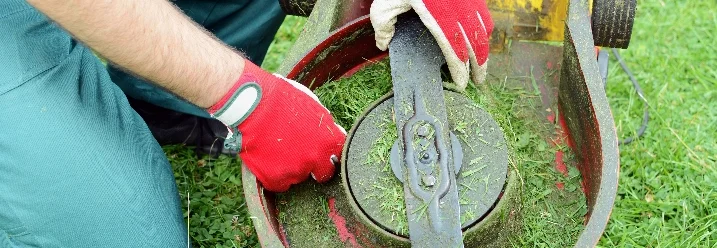 Person reinigt Rasenmäher mit Handschuhen